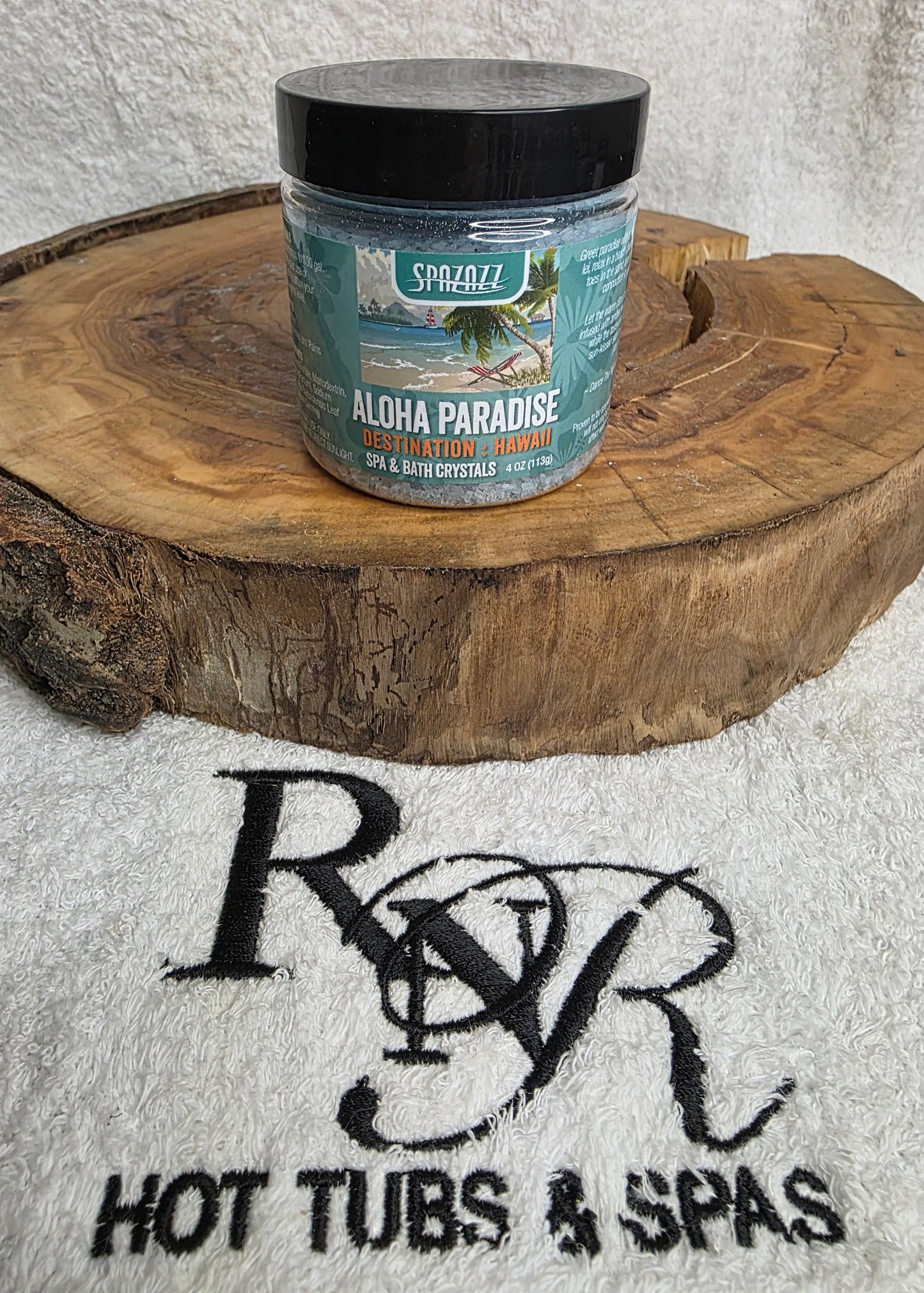Container of Aloha Paradise aromatherapy crysals on a wooden block with RnR Hot Tubs & Spas branding in the background.