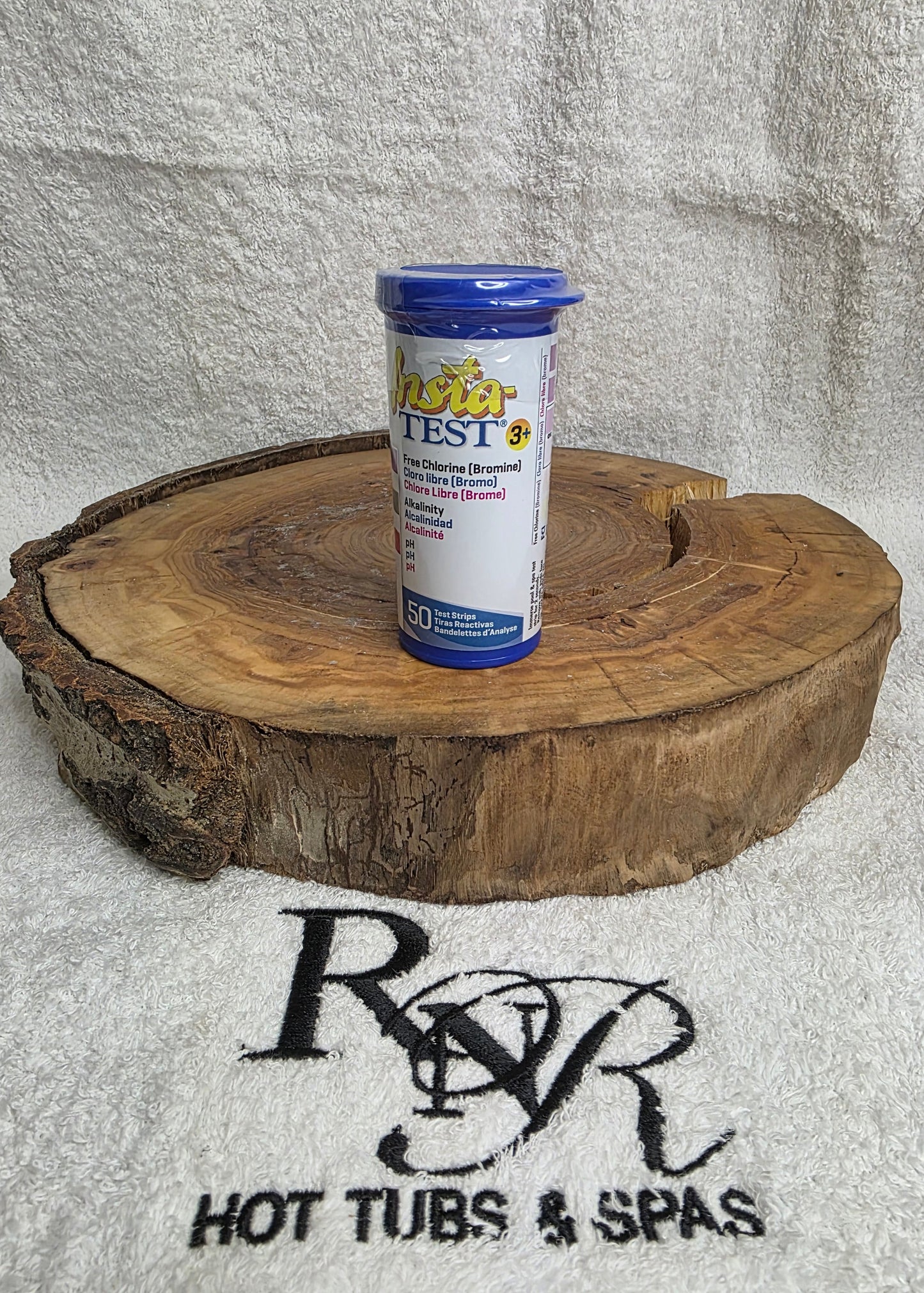 Bottle of pool test strips on a wooden disc with RnR Hot Tubs & Spas logo in the background.