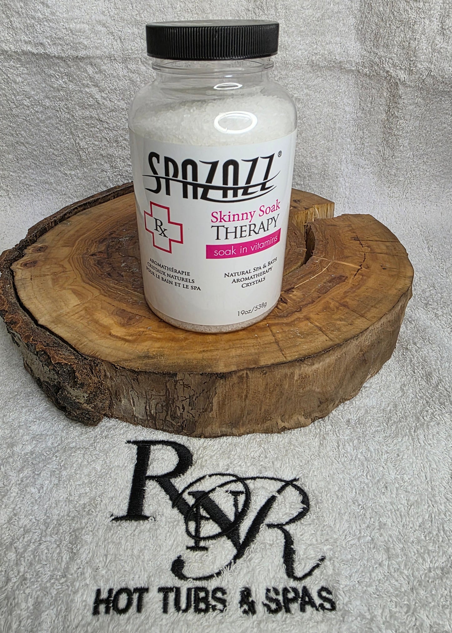 Bottle of Spazazz Skinny Soak aromatherapy crystals on a wooden block with RnR Hot Tubs & Spas logo in the background